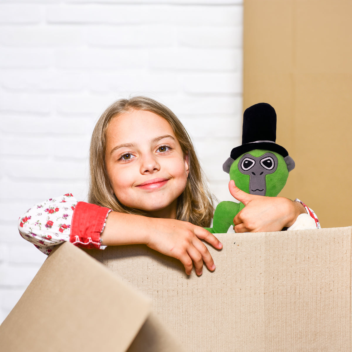 Girl peeking out of a cardboard box holding the green long arm monkey plush