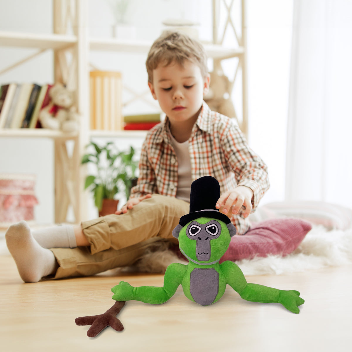Boy sitting on a bedroom rug reaching for the green long arm monkey plush in its top hat