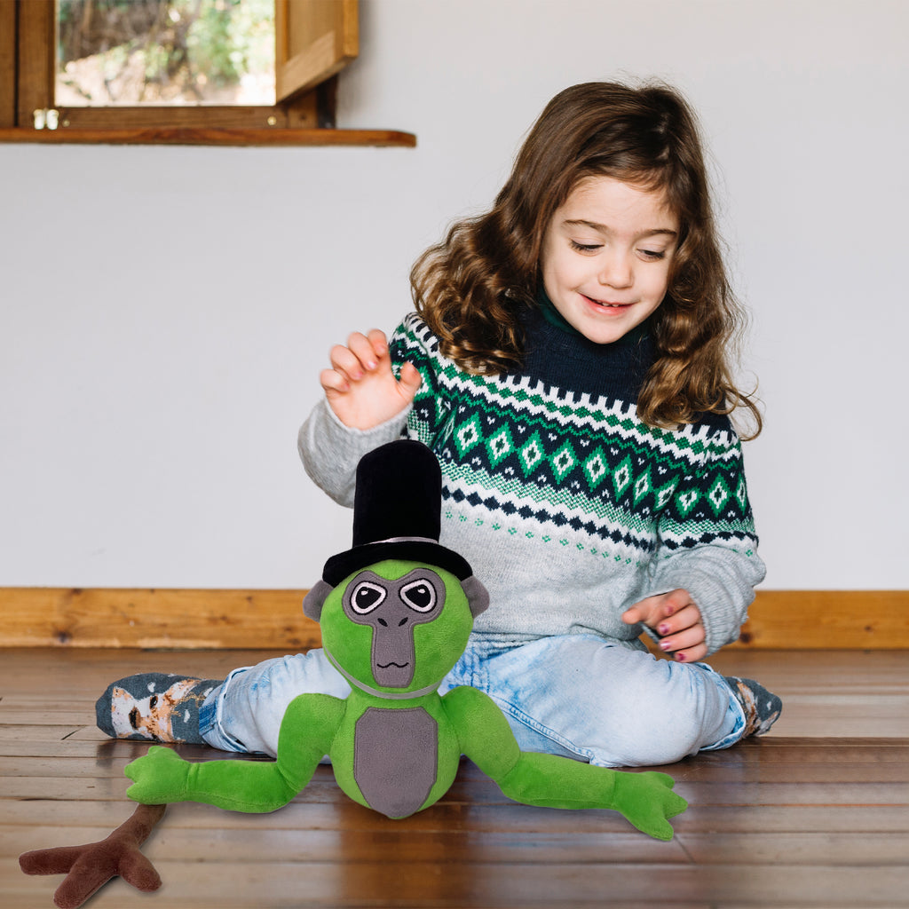 Girl in a knit sweater sitting on a wooden floor with the green long arm monkey plush